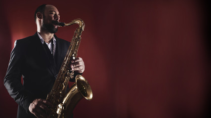 Portrait of professional musician saxophonist man in  suit plays jazz music on saxophone, red...