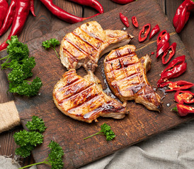 pork fried steak on the rib lies on a vintage brown wooden board, next to fresh red chili peppers, top view
