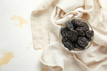 Bowl with tasty prunes on light background