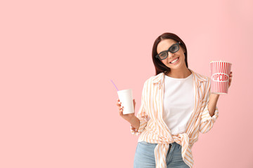 Young woman with popcorn and drink watching movie on color background