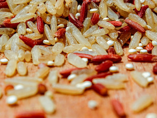 Mix red rice, complete rice, quinoa uncooked on wooden spoon and wooden surface 