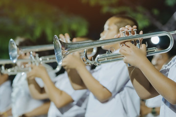 Male student with friends blow the trumpet with the band for performance on stage at night.
