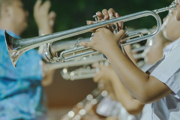 Male student with friends blow the trumpet with the band for performance on stage at night. © JinnaritT