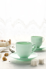 Obraz na płótnie Canvas Mint colored tea cups, sugar bowl on a table by window