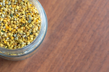 glass vase full of bee pollen granules, seen from above on a dark wooden table.