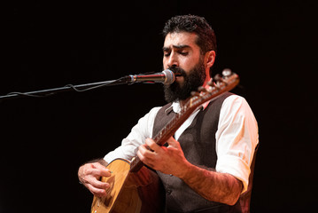 Good-looking man with a thick black beard, musician playing a typical stringed instrument on stage, the tembur