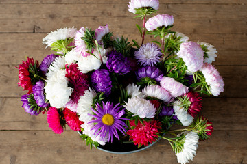 large lush bouquet of colourful asters: white, pink, purple, red, burgundy in a tin bucket on a wooden floor background, top view