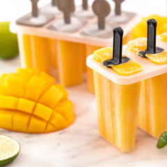 Fresh mango fruit popsicle ice in the plastic shaping box on bright marble table. Summer mood...