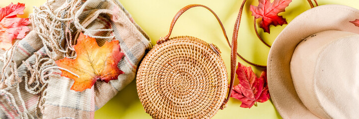 Multicolored autumn background. Women's felt hat, wicker bag, checkered plaid, autumn red yellow leaves. Yellow background, top view, wide composition. Autumn fashion, cozy fall concept, flatlay