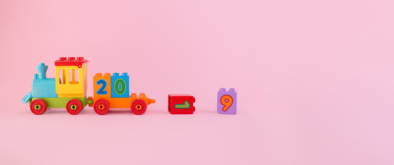 Fototapeta na wymiar Colorful toy train isolated on pink background with dropped numbers 1 and 9 symbolizes outgoing 2019 year with place for text