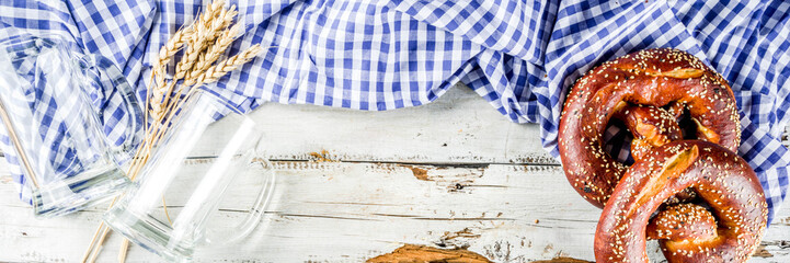Oktoberfest festive background with traditional Bavarian checkered tablecloth, pretzels and beer mugs.