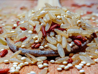 Mix red rice, complete rice, quinoa uncooked on wooden spoon and wooden surface 