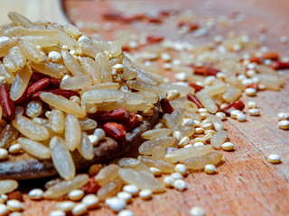 Mix red rice, complete rice, quinoa uncooked on wooden spoon and wooden surface 