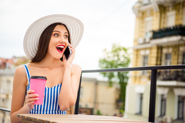 Pretty lady speaking over telephone hear great news sitting in cozy street cafe wear sun hat and...