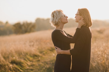 Samesex caucasian lesbian couple outdoors on the background of beautiful nature. Young stylish women hugging at sunset, affectionate and happy.