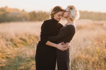 Samesex caucasian lesbian couple outdoors on the background of beautiful nature. Young stylish women hugging at sunset, affectionate and happy. - obrazy, fototapety, plakaty