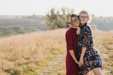 Samesex caucasian lesbian couple outdoors on the background of beautiful nature. Young stylish women hugging at sunset, affectionate and happy.