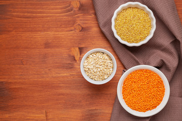 Raw red lentils, , bulgur, oak flakes in white bowls.