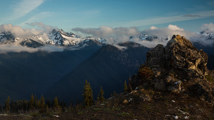 Olympic mountains in clouds in the background with a rocky peak in the foreground