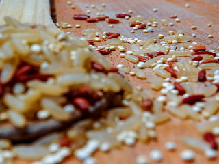 Mix red rice, complete rice, quinoa uncooked on wooden spoon and wooden surface 
