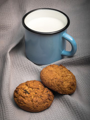 Blue enamel mug with milk and paires of biscuits on grey textile background