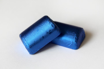 A pile of chocolate candies wrapped in blue foil isolated on white surface. Template for greeting...