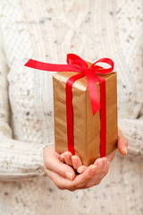 Woman holding a gift box tied with red ribbon in the hands