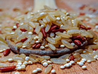 Mix red rice, complete rice, quinoa uncooked on wooden spoon and wooden surface 