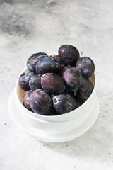 Juicy plums in white dishes on a light grey table