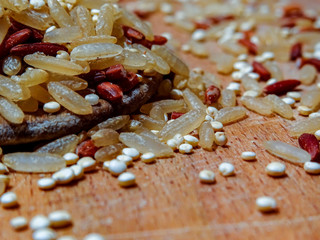 Mix red rice, complete rice, quinoa uncooked on wooden spoon and wooden surface 