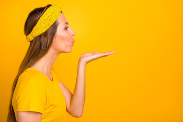 Profile side photo of lovely millennial sending air kisses at copy space isolated over yellow background