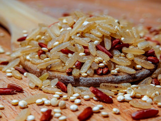 Mix red rice, complete rice, quinoa uncooked on wooden spoon and wooden surface 