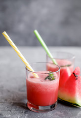 Glass of fresh watermelon lemonade with green leaf of mint at the gray cement background