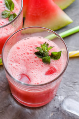 Glass of fresh watermelon lemonade with green leaf of mint at the gray cement background