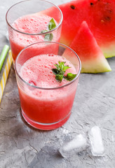 Glass of fresh watermelon lemonade with green leaf of mint at the gray cement background