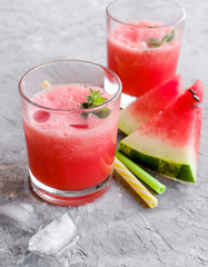 Glass of fresh watermelon lemonade with green leaf of mint at the gray cement background