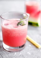 Glass of fresh watermelon lemonade with green leaf of mint at the gray cement background