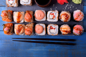 Sushi rolls assortment served on slate plate and chopsticks on blue table