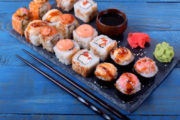 Sushi rolls assortment served on slate plate and chopsticks on blue table