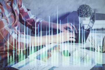 Double exposure of stock graph with businessman typing on computer in office on background. Concept of hard work.