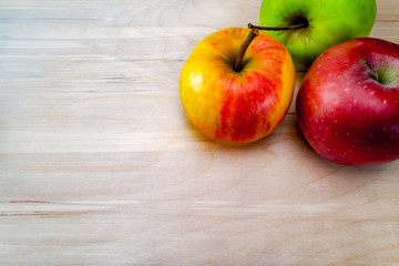 Fresh, red, green and yellow-red apples on a wooden table, the background is a table made of light oak. free space for text