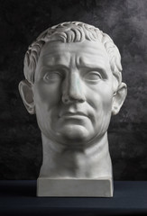 Gypsum copy of ancient statue Augustus head on dark textured background. Plaster sculpture man face.