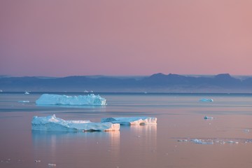 Arctic nature landscape with icebergs in Greenland icefjord with midnight sun sunset / sunrise in...
