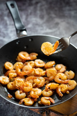 Tasty appetizing juicy peeled fried shrimp in a pan close-up with one shrimp on a fork.