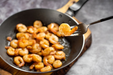 Tasty appetizing juicy peeled fried shrimp in a pan close-up with one shrimp on a fork.