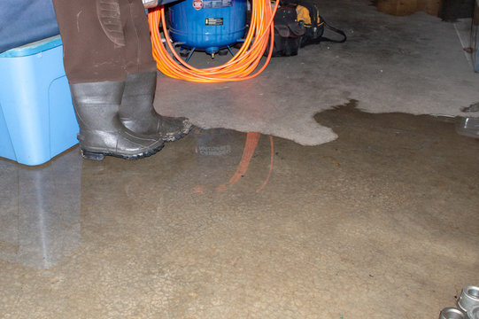 A pair of hip boots, a tote and various items stored in the basement are about to be soaked in leaking water. Some professional waterproofing is needed. Bokeh.