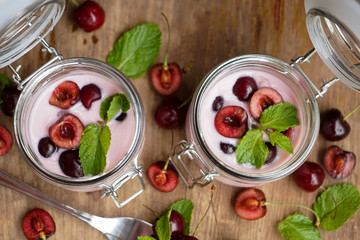 selective focus, still life, Breakfast. cherry pink yogurt in a glass jar with ripe cherries and green mint leaves