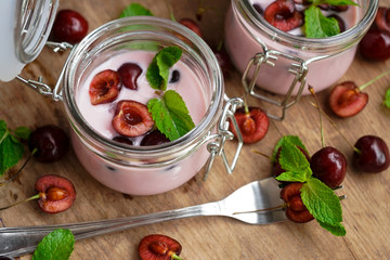 selective focus, still life, Breakfast. cherry pink yogurt in a glass jar with ripe cherries and green mint leaves