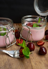selective focus, still life, Breakfast. cherry pink yogurt in a glass jar with ripe cherries and green mint leaves