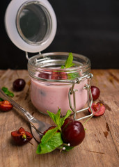 selective focus, still life, Breakfast. cherry pink yogurt in a glass jar with ripe cherries and green mint leaves